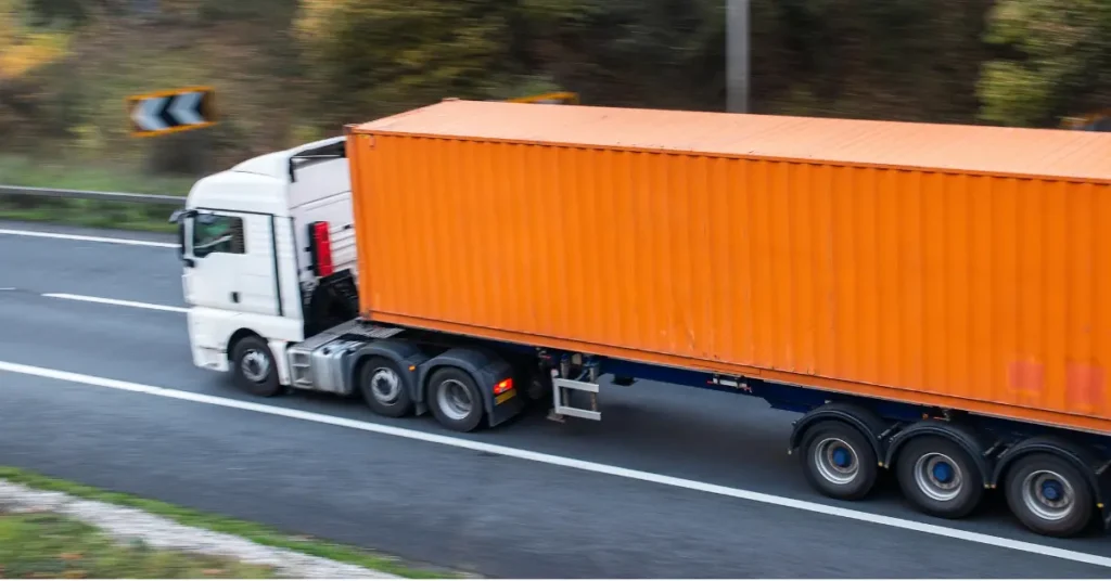 Portable storage container being transported by a white truck with an orange container on a highway