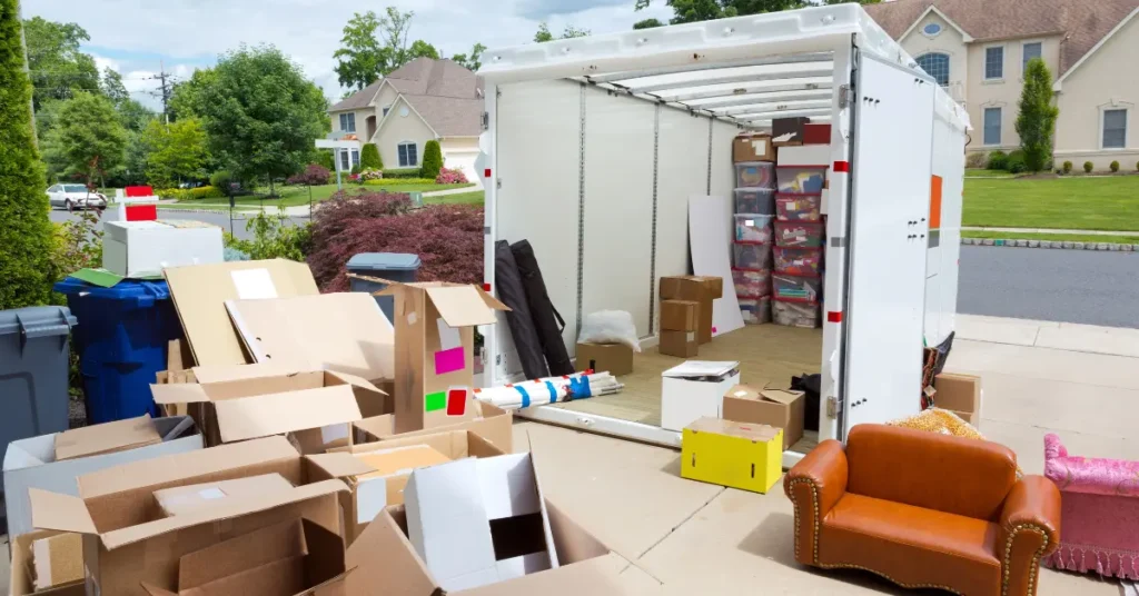 Portable storage container on a residential driveway surrounded by boxes and furniture, ideal for renting storage containers